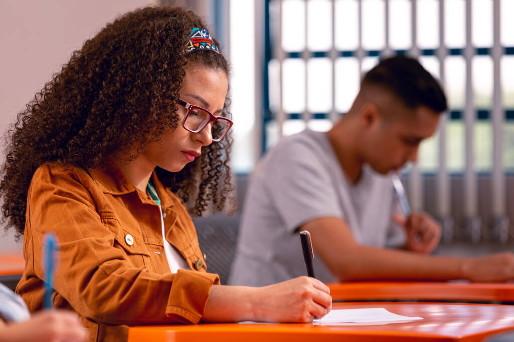 Homem e mulher em sala de aula, resolvendo exercícios de verbos abundantes.