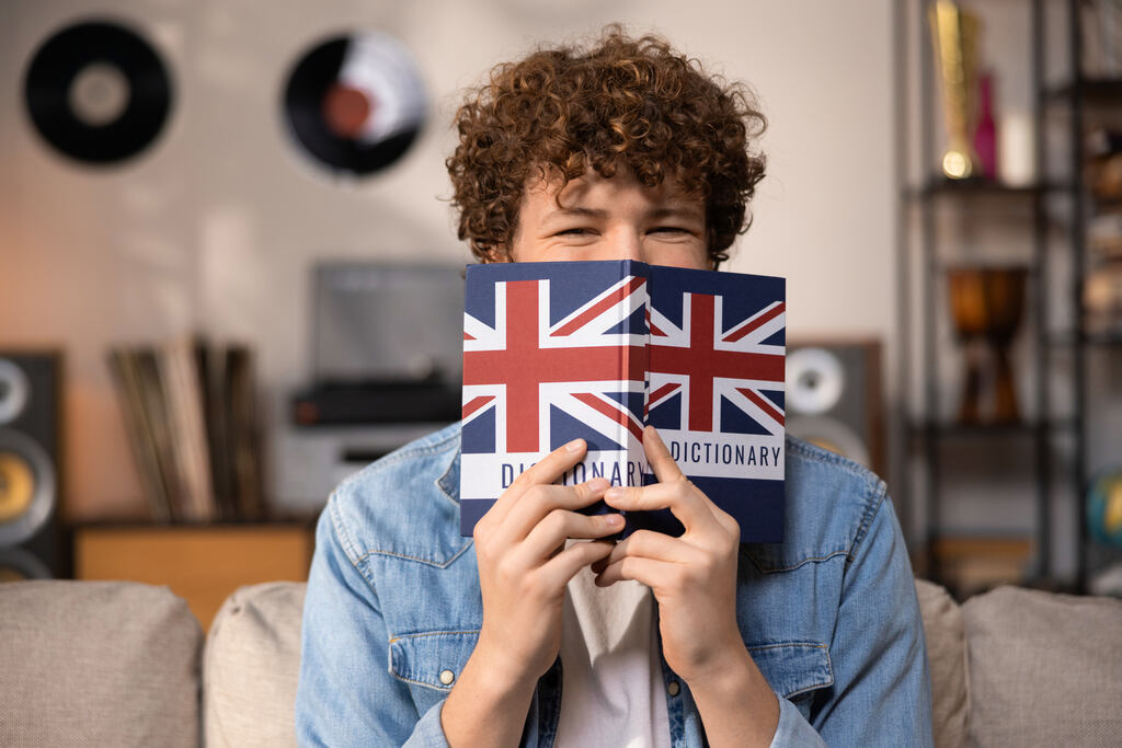 Homem segurando dicionário de inglês em frente ao rosto, estudando exemplos de there is e there are.
