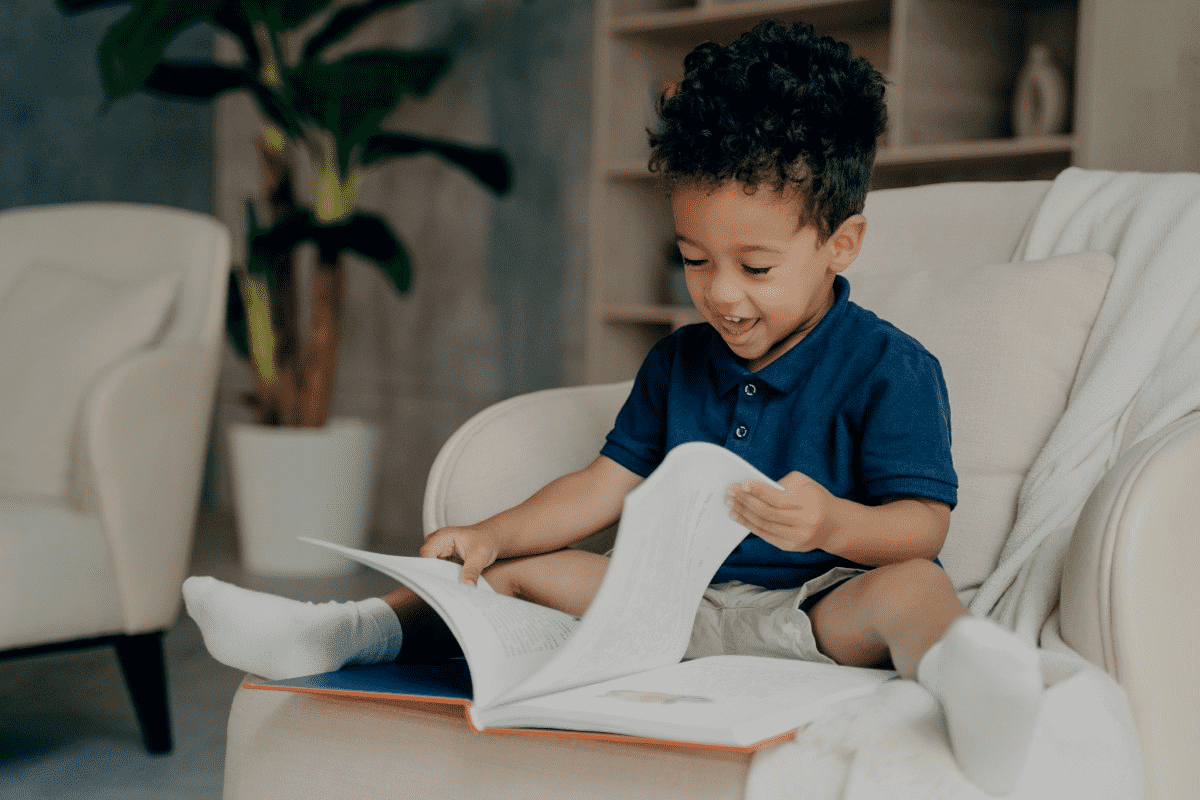 Foto de menino sorridente lendo livro. Como ensinar a ler é algo importante para a criança, saiba como fazer.