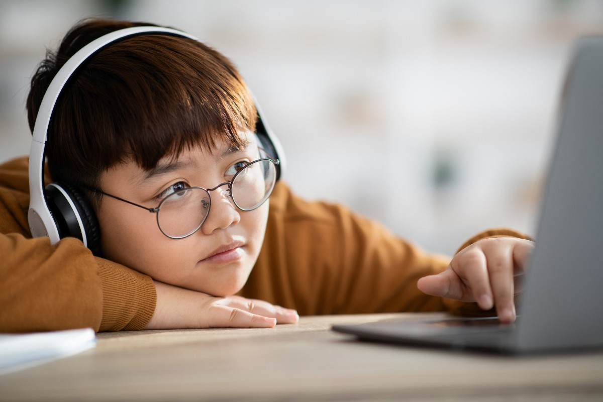 Foto de menino de fone de ouvidos, desanimado, mexendo no computador. A educação infantil na pandemia foi muito prejudicada pelo isolamento.